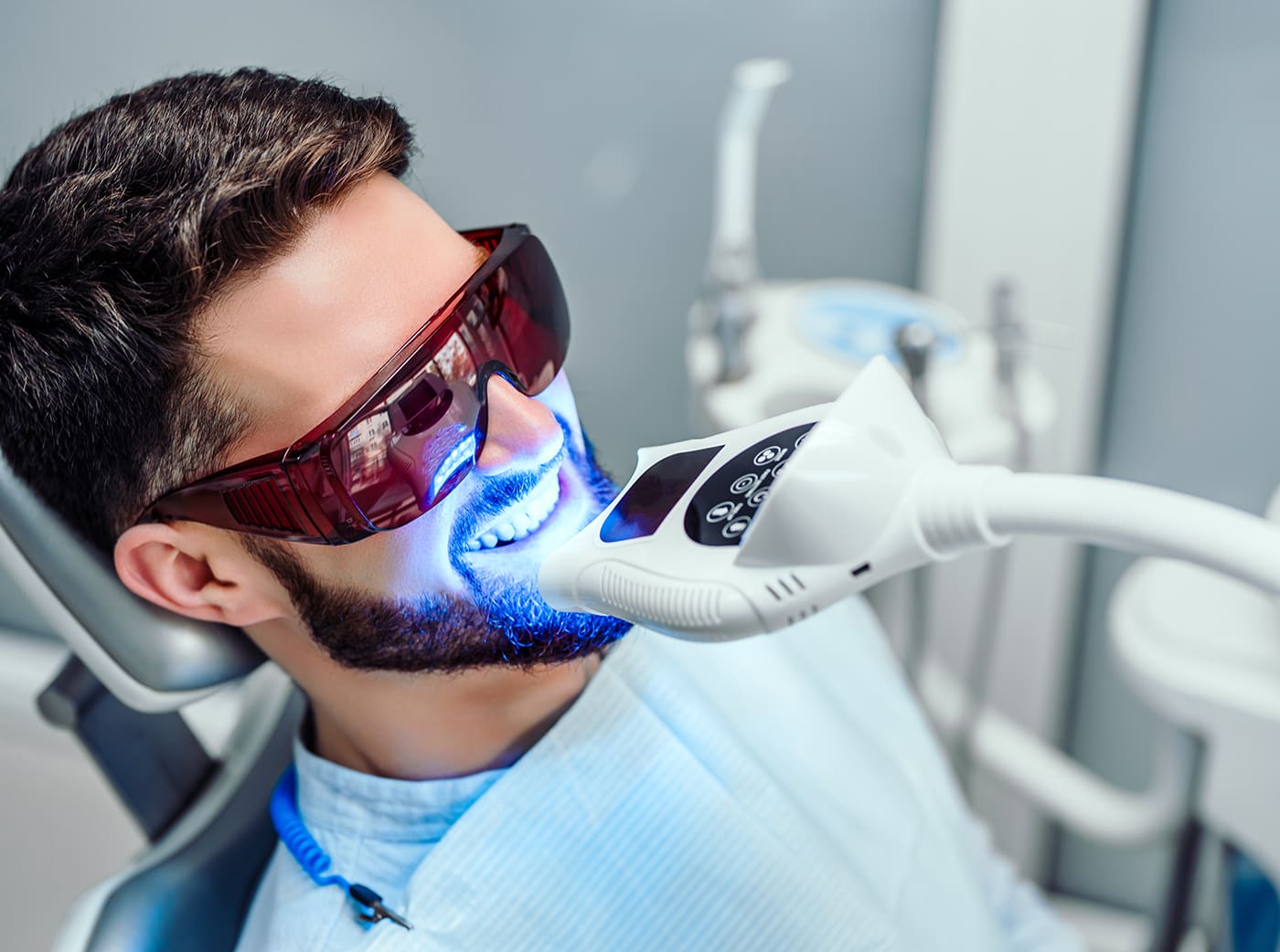 Dentist starting teeth whitening procedure with young man.
