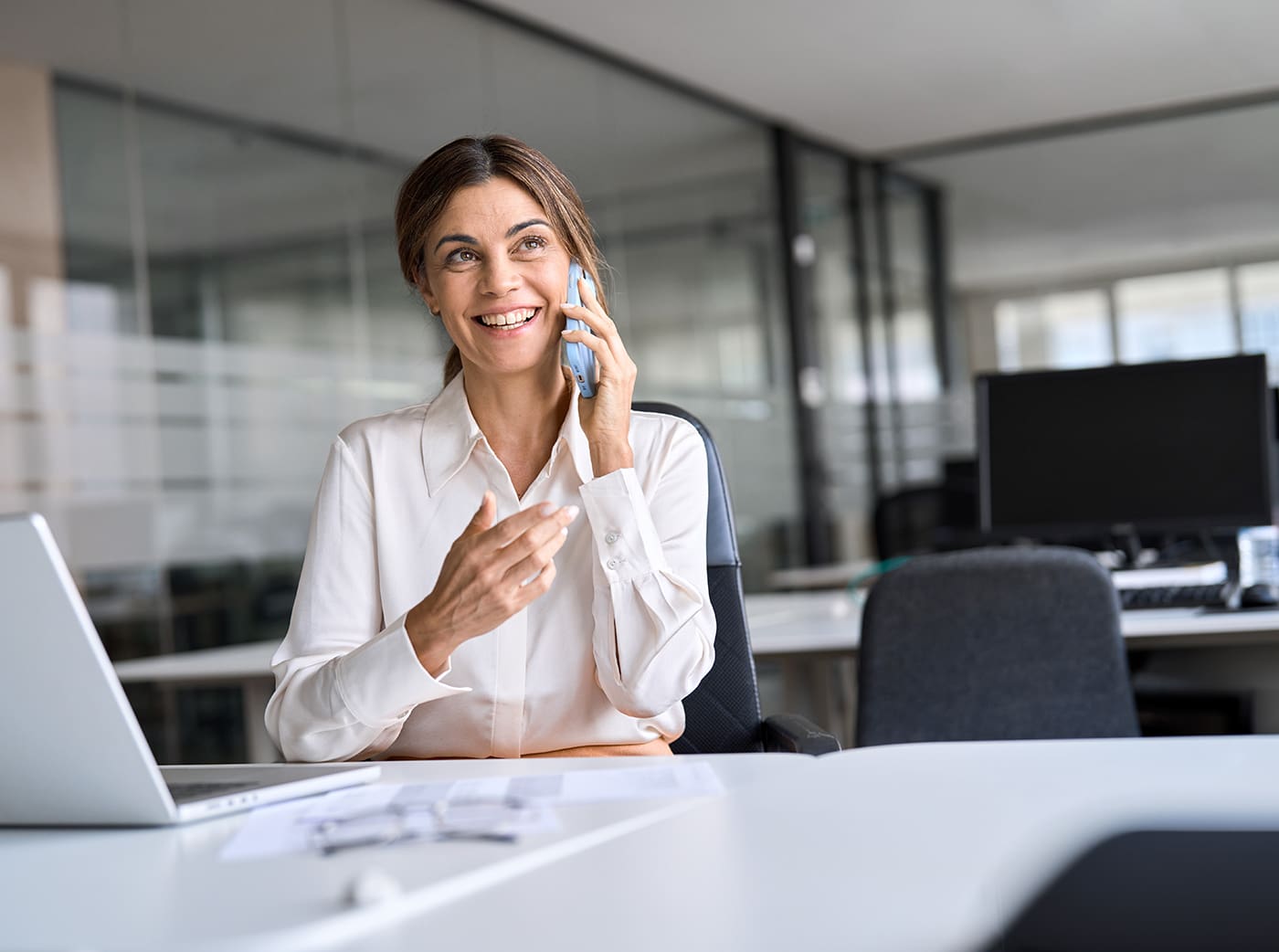 Happy middle aged woman talking on phone making call in office.